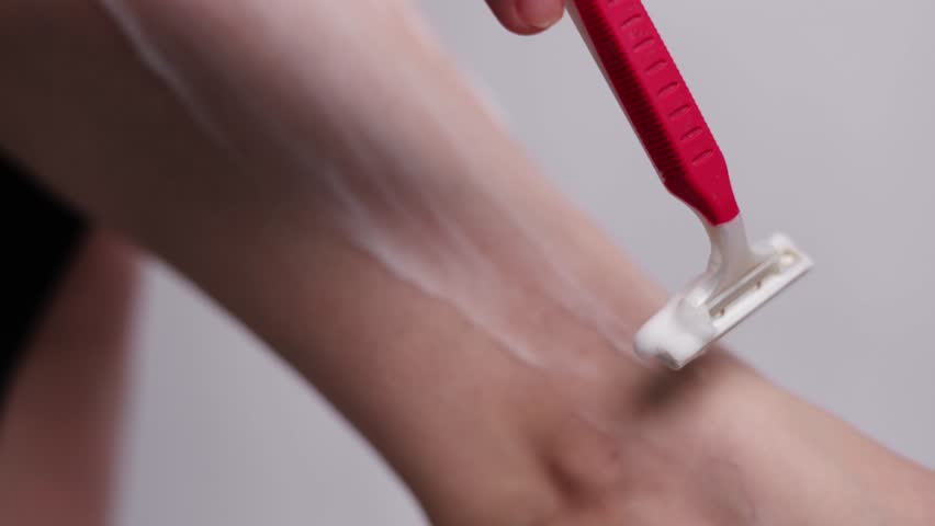 Process of removing hair with pink razor from leg covered in soapy foam
