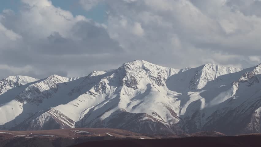 Snow-Covered Mountain Peaks Shrouded in Clouds Against Blue Sky