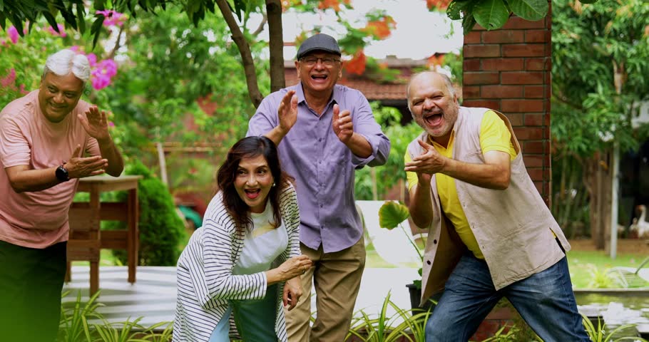 Senior friends enjoying throwing  flying disc in garden, Indian asian old friends smiling and laughing together while celebrating reunion in lush green nature setting