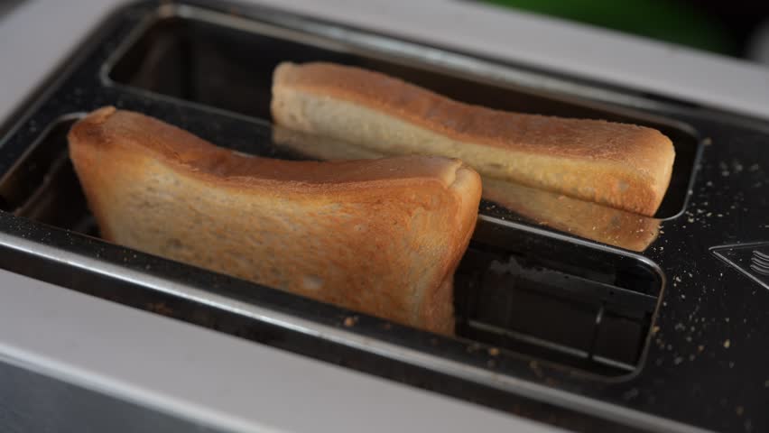 Bread slices gradually browning inside electric toaster, transforming into crispy golden toast for morning breakfast preparation