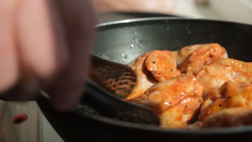 A cook uses tongs to flip golden chicken drumsticks and wings sizzling in hot oil. Juicy pieces frying in a pan for perfect crisp and even cooking. Street food or homemade comfort meal.