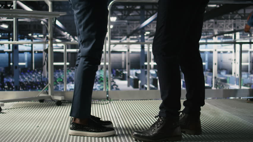 Data center team leader and worker reviewing performance dashboards of AI equipment rigs. Server room supervisor oversees programmer examining machine learning algorithms on screen, camera A