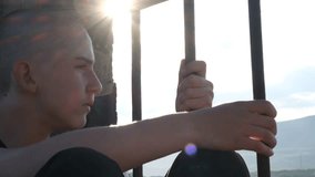 Warm sunset light shines into a prison cell as a sweet teenage boy gazes through the bars, lost in thought. Wrongfully convicted, he sits in silence trapped by a broken system, too young for such fate - Powered by Shutterstock - Get 15% off with code: PIKWIZARD15