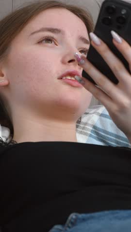 Young woman relaxing on comfortable sofa talking on hands-free smartphone making expressive hand gestures in relaxed home environment recording voice message vertical video