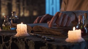 Person slowly tracing lines of old book with their finger in candlelit room, surrounded by small potion bottles on stone table, evoking sense of ancient magic and mystery in medieval stone interior. - Powered by Shutterstock - Get 15% off with code: PIKWIZARD15