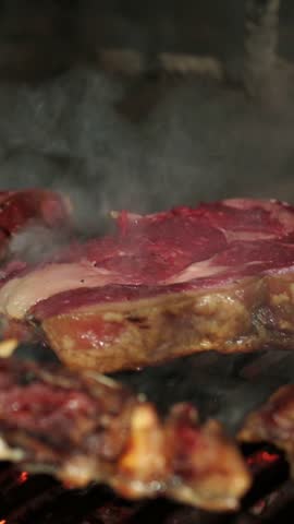 Delicious ribeye steak grilling on a hot charcoal grill, smoke rising, in a restaurant kitchen setting