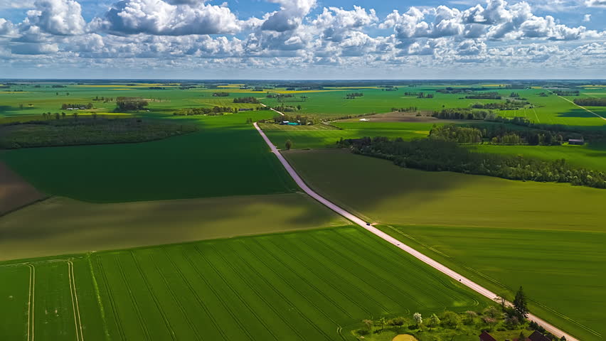 Green crops growing in farmland fields in a rural landscape with clouds drifting across the sky casting shadows on the landscape - forward aerial cloudscape hyper lapse