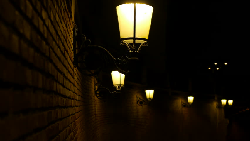 Vintage street light on a brick wall is illuminating the night. The light creates a warm glow, contrasting with the darkness surrounding it