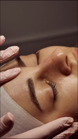 Beautician doing female anti-wrinkle rejuvenating facial massage in beauty salon, close-up, vertical