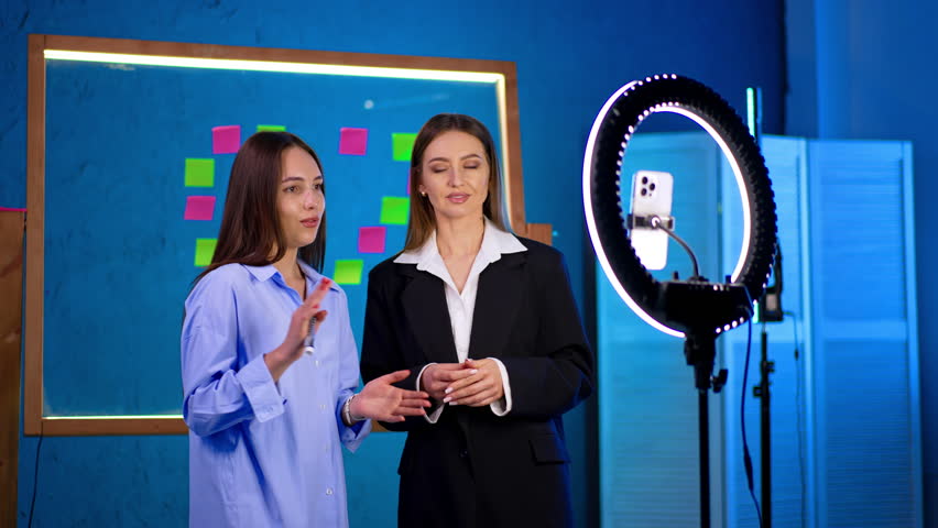 Positive Caucasian female bloggers speak to phone camera with ring light. Blog content creation.