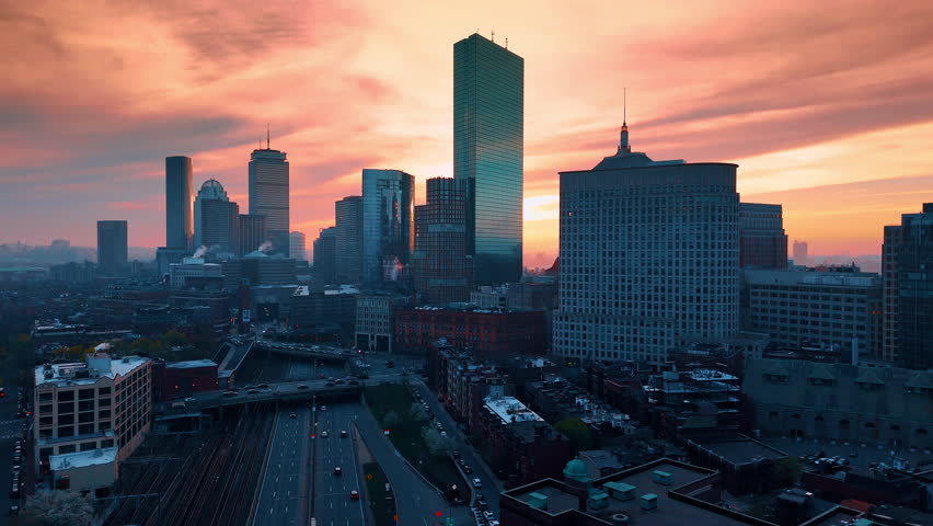 Stunning skyline of modern Boston, Massachusetts, USA at the backdrop of pink cloudy sky. Drone footage above the lively city at dusk.