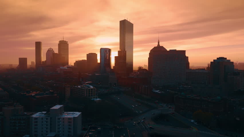 Transport runs by the roads of the dark city at dusk time. Orange sky is at backdrop of Boston skyline at sunset.