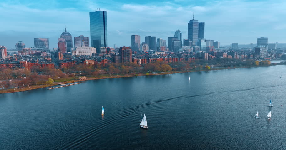 Beautiful sailboats move smoothly by the waterscape of the Charles River. Diverse skyline of Boston, Massachusetts, USA on the waterfront. Aerial perspective.