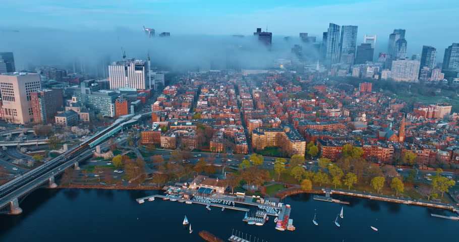 Multiple cars move by the roads on the waterfront of the Charles River. Downtown of Boston is covered with smoke. Air pollution in metropolis. Aerial perspective.