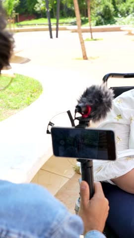 Woman journalist conducting upbeat interview with wheelchair user in sunny park, capturing personal story and disability representation with professional approach