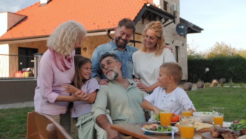 Happy multigenerational family posing for photos at a table in their backyard, enjoying lunch together
