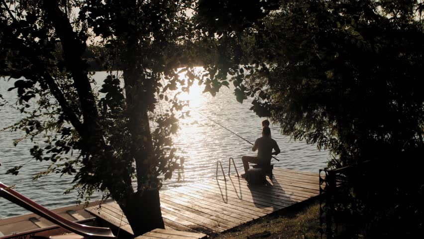 Silhouette of a fisherman casting a line at sunset, creating a tranquil scene of outdoor recreation