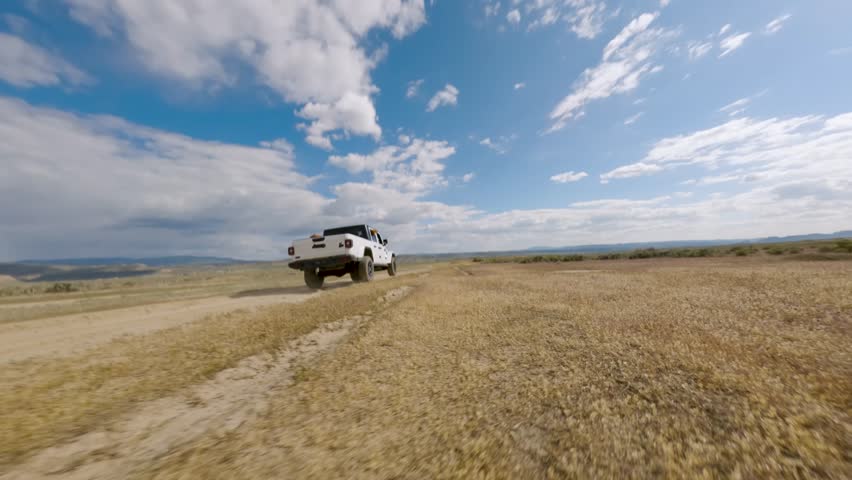 FPV Drone Tracking Shot Behind Pickup Truck on Dirt Road – Black Labrador Running Alongside and Golden Retriever Watching from Truck Bed, Revealing Desert Landscape
