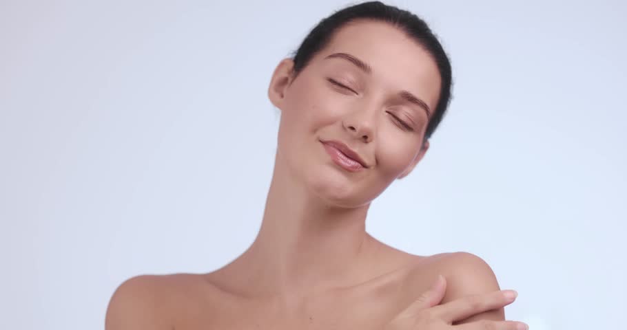 Graceful woman caresses shoulders and collarbone with soft touch, eyes closed in serenity. Ideal for beauty, skin care, wellness, personal care and feminine elegance promotional content.