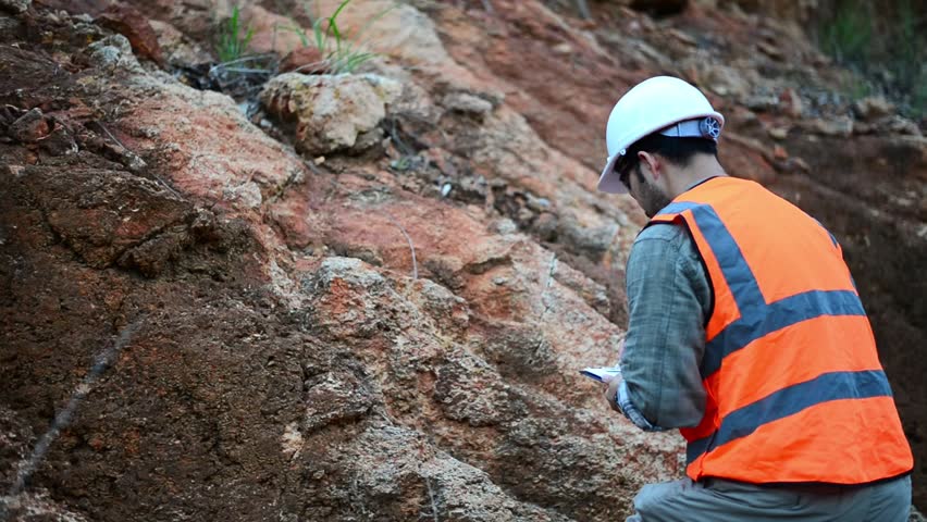 A geologist is examining minerals in the layers of rock on a mountain.