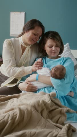 Vertical shot of mature Caucasian woman visiting her daughter during postpartum recovery time in modern maternity hospital
