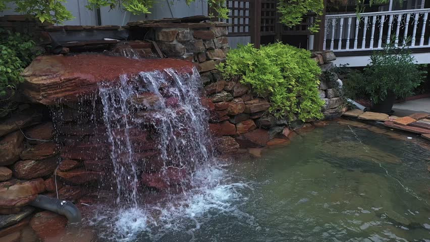 Backyard Waterfall Flowing Over Stacked Rocks Into Clear Pond In Atlanta, Georgia. panning shot