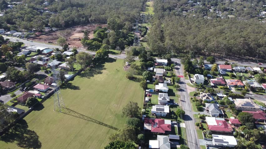 4K Aerial view of a green park with high voltage powerlines passing through and private homes each side of the park