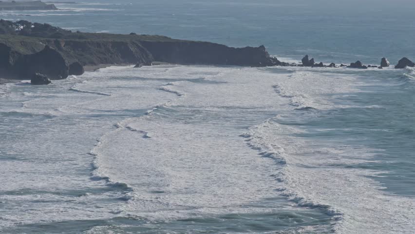 Aerial view of waves breaking in rhythmic curves along the rugged Big Sur coast, highlighting the natural power and beauty of California’s shoreline.
