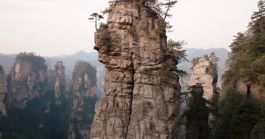 Close aerial view of a towering sandstone pinnacle with sparse trees growing on top, surrounded by cliffs in Zhangjiajie National Park