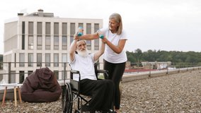 Senior woman assists elderly husband exercising with dumbbells while wheelchair bound, outdoor setting showcases mutual support and healthy lifestyle promotion despite physical limitations. - Powered by Shutterstock - Get 15% off with code: PIKWIZARD15