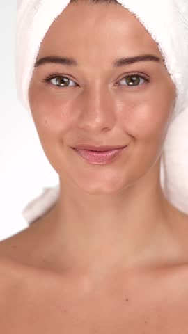 Beautiful young Caucasian woman removes makeup with a wet wipe, wrapped in a towel, promoting clean skin and wellness. Concept for beauty, skincare, spa and cosmetic product ads.