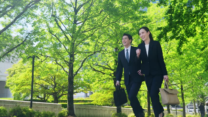 Male and female business people running through a city with fresh greenery