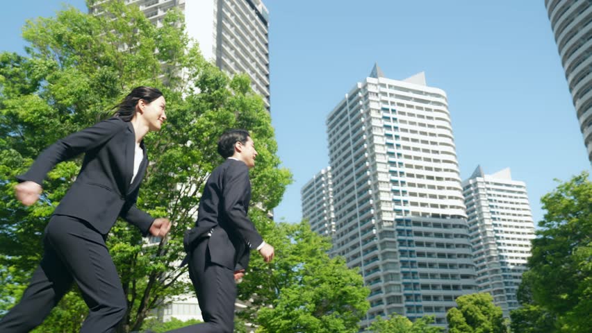 Male and female business people running through a city with fresh greenery