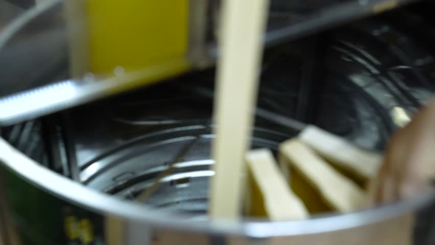 Person Putting The Hive Frames On Cylindrical Honey Extractor Machine. - closeup shot