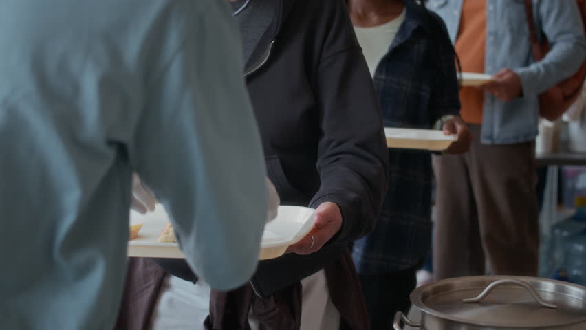 Handheld shot of diverse group of refugees getting food from volunteer in aid center