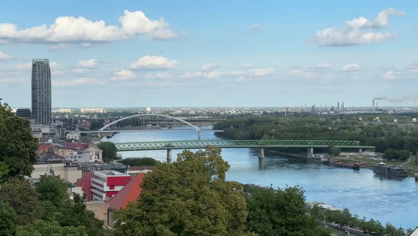 Bratislava, Slovakia - 05162025: Bratislava, View of SNP Bridge in Bratislava with moving traffic, UFO observation tower above, Petržalka residential area, and the Danube River in the foreground.