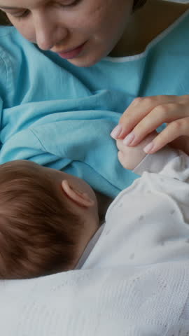 High angle view of happy young woman touching hand of her newborn baby while breastfeeding in maternity hospital room