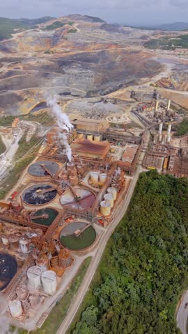 Expansive backward aerial at Barrick Gold mine in Cotuí, Dominican Republic, with industrial tanks, smokestacks, roads, and a vast open-pit mine. Vertical shot