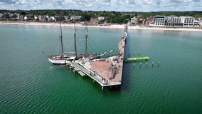 Aerial footage of sailing ship docked at the long pier in Scharbeutz on the Baltic Sea, with pan and retreat movement of the camera. Wooden pier with three-masted sailing vessel at seaside resort. - Powered by Shutterstock - Get 15% off with code: PIKWIZARD15
