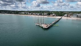 Aerial view of tall ship moored at long pier in Scharbeutz, coastal resort on the Baltic Sea in Schleswig-Holstein, Germany. The camera retreats and pans right to left, revealing seaside town. - Powered by Shutterstock - Get 15% off with code: PIKWIZARD15