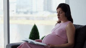 Expectant mother holds book on knees while talking to husband through headphones. Woman looks serious. Sunlight from window lights room - Powered by Shutterstock - Get 15% off with code: PIKWIZARD15