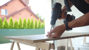 Man in work overalls bib using cordless power drill to make hole in laminated wood board. Male carpenter working in home workshop, drilling chipboard on workbench - Powered by Shutterstock - Get 15% off with code: PIKWIZARD15