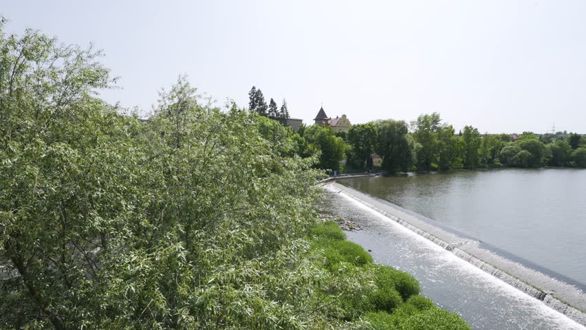A broad river with a weir runs through a rural area on a sunny day - top view