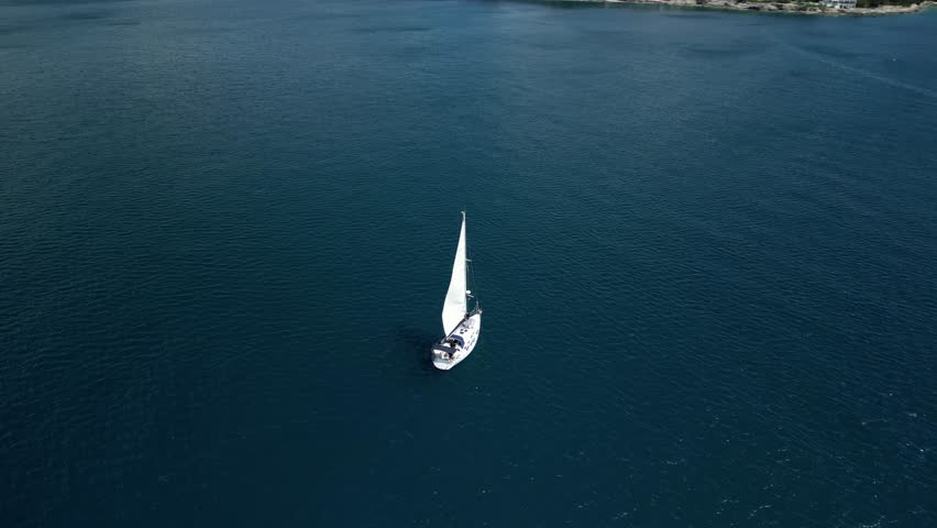 An orbiting aerial view of a sailboat sailing along the Adriatic Sea off the shore of Verudela region of Pula, Croatia on a sunny day
