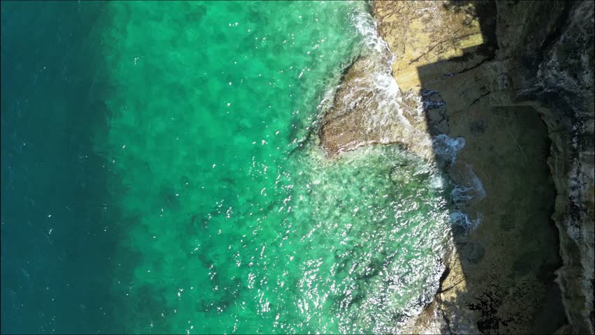 A bird's eye drone footage of the Adriatic Sea waves gently lapping on the rocky coastline of Pula city in Istrian Peninsula, Croatia on a sunny day