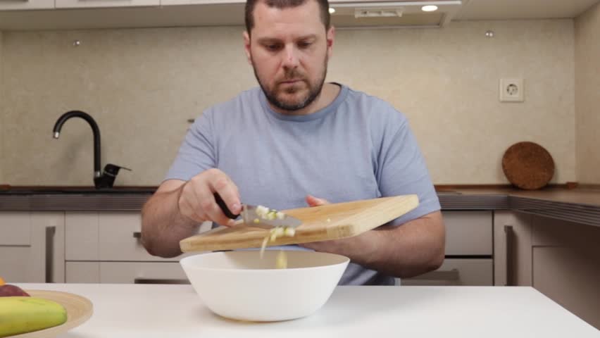 man adding sliced ​​pear to bowl of fruit salad