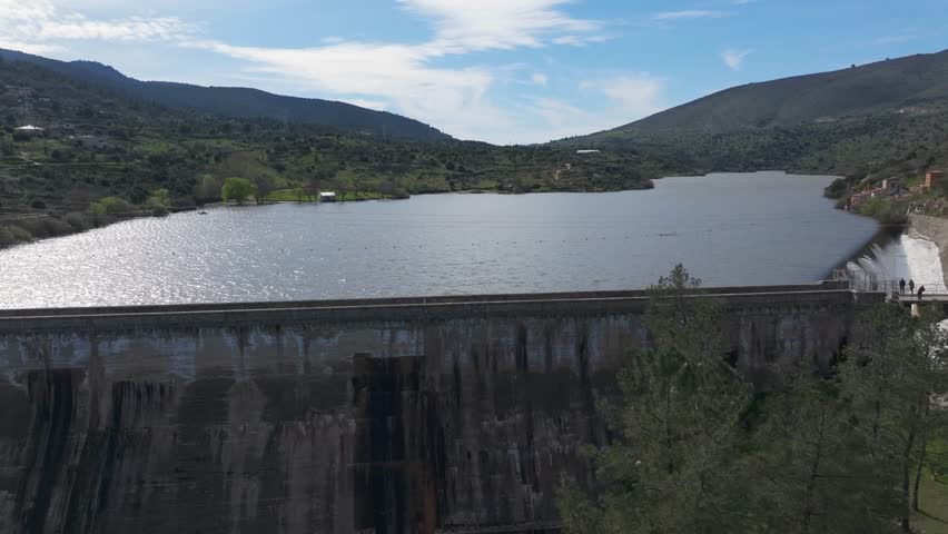 Lateral drone flight along a fully loaded dam wall. Sunlight reflects on the water
