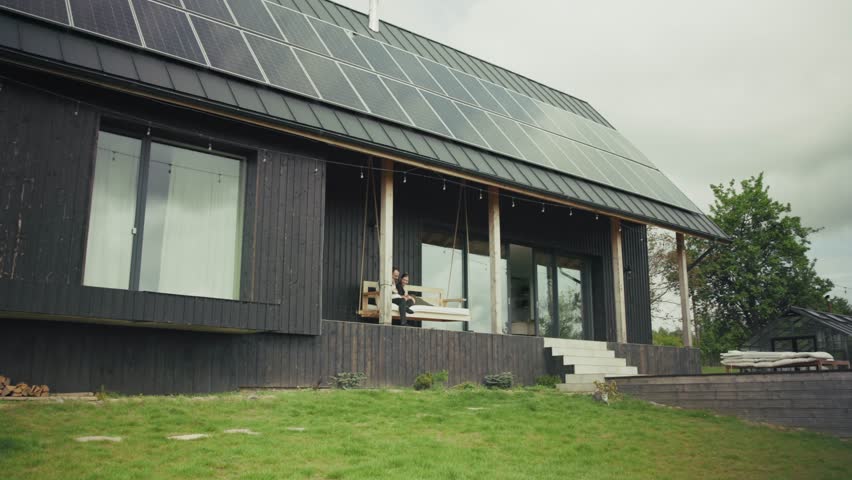 Family enjoys time together on a porch swing of their modern, eco-friendly home with solar panels