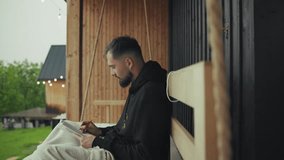 Young man enjoys working remotely from the comfort of a porch swing at his modern mountain cabin - Powered by Shutterstock - Get 15% off with code: PIKWIZARD15