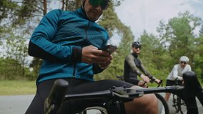 Man in activewear holds smartphone sitting on bicycle against teammates on road. Young cyclists rest during vehicle racing at summer forest countryside - Powered by Shutterstock - Get 15% off with code: PIKWIZARD15